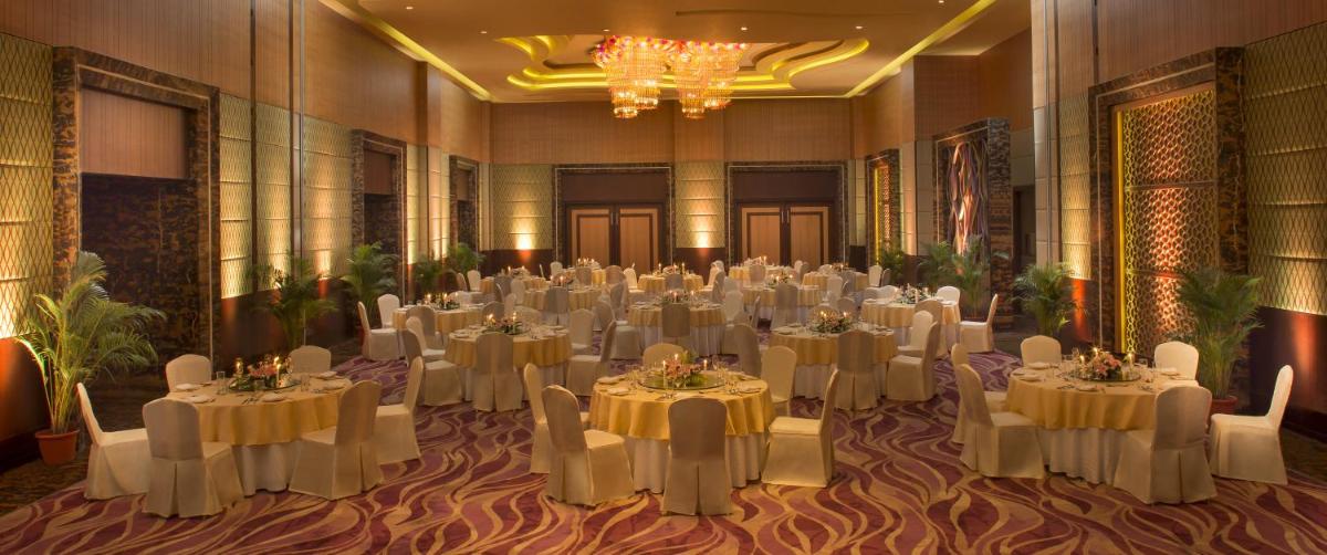 a banquet hall with white tables and chairs and a chandelier at Radisson Blu Hotel, Indore in Indore