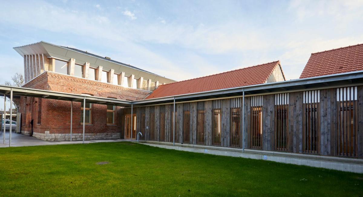 Vue extérieure d'un bâtiment en briques avec une pelouse dans l'établissement La Ferme Des Ailleurs, à Arleux-du-Nord