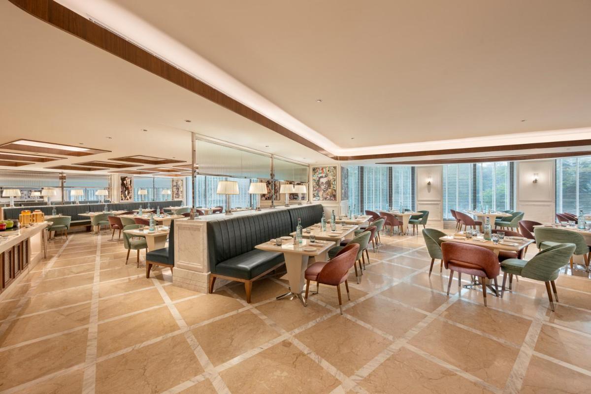 a restaurant with tables and chairs and windows at Aurika, Mumbai International Airport - Luxury by Lemon Tree Hotels in Mumbai a restaurant with tables and chairs and windows at Aurika, Mumbai International Airport - Luxury by Lemon Tree Hotels in Mumbai