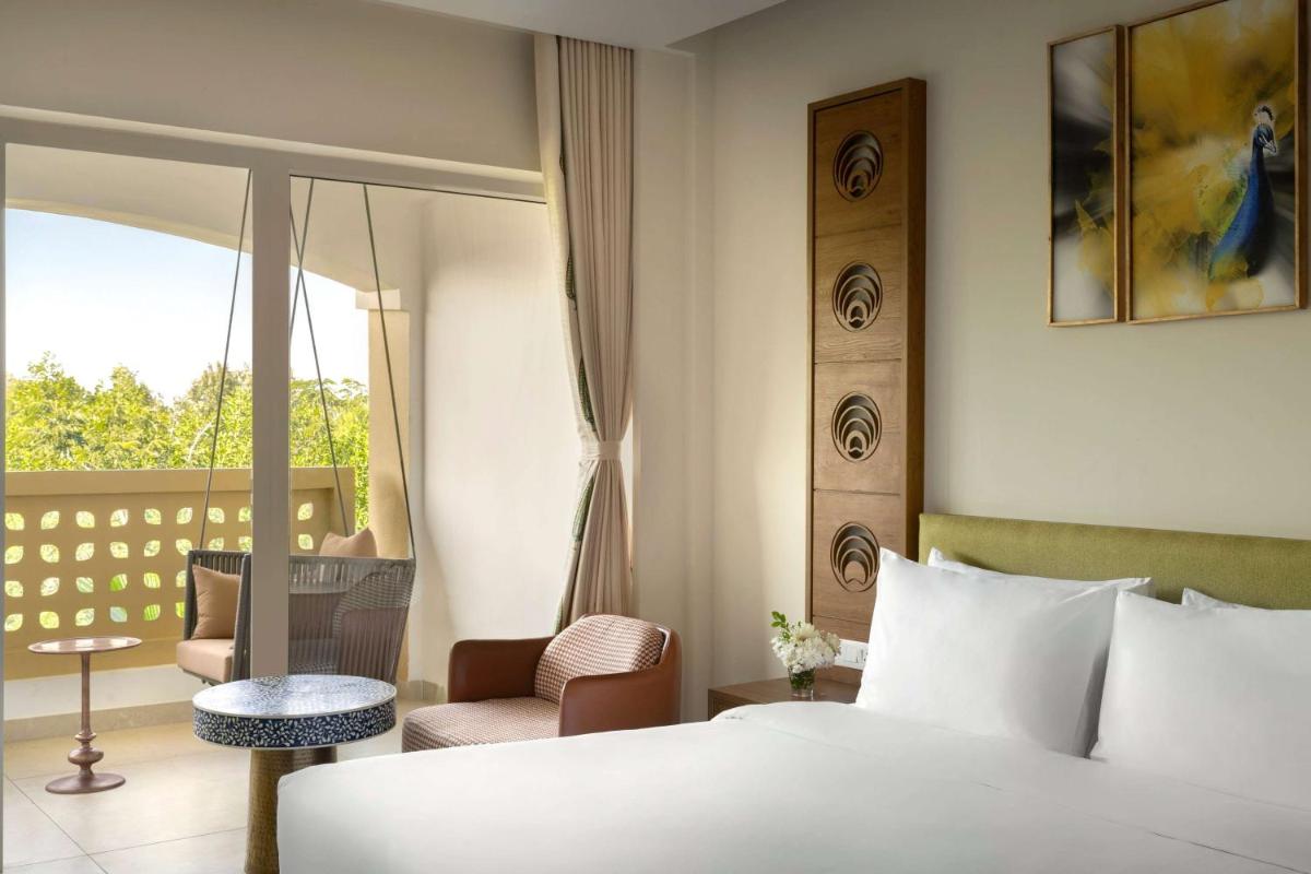 a hotel room with a bed and a balcony at Hawthorn Suites by Wyndham Dwarka in Dwarka a hotel room with a bed and a balcony at Hawthorn Suites by Wyndham Dwarka in Dwarka