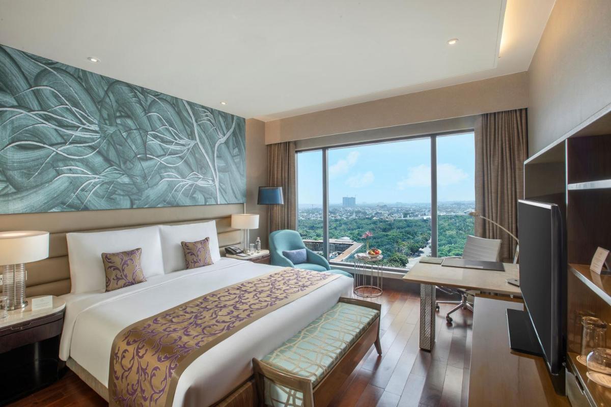 a hotel room with a bed and a desk and a window at The Leela Ambience Convention Hotel Delhi in New Delhi