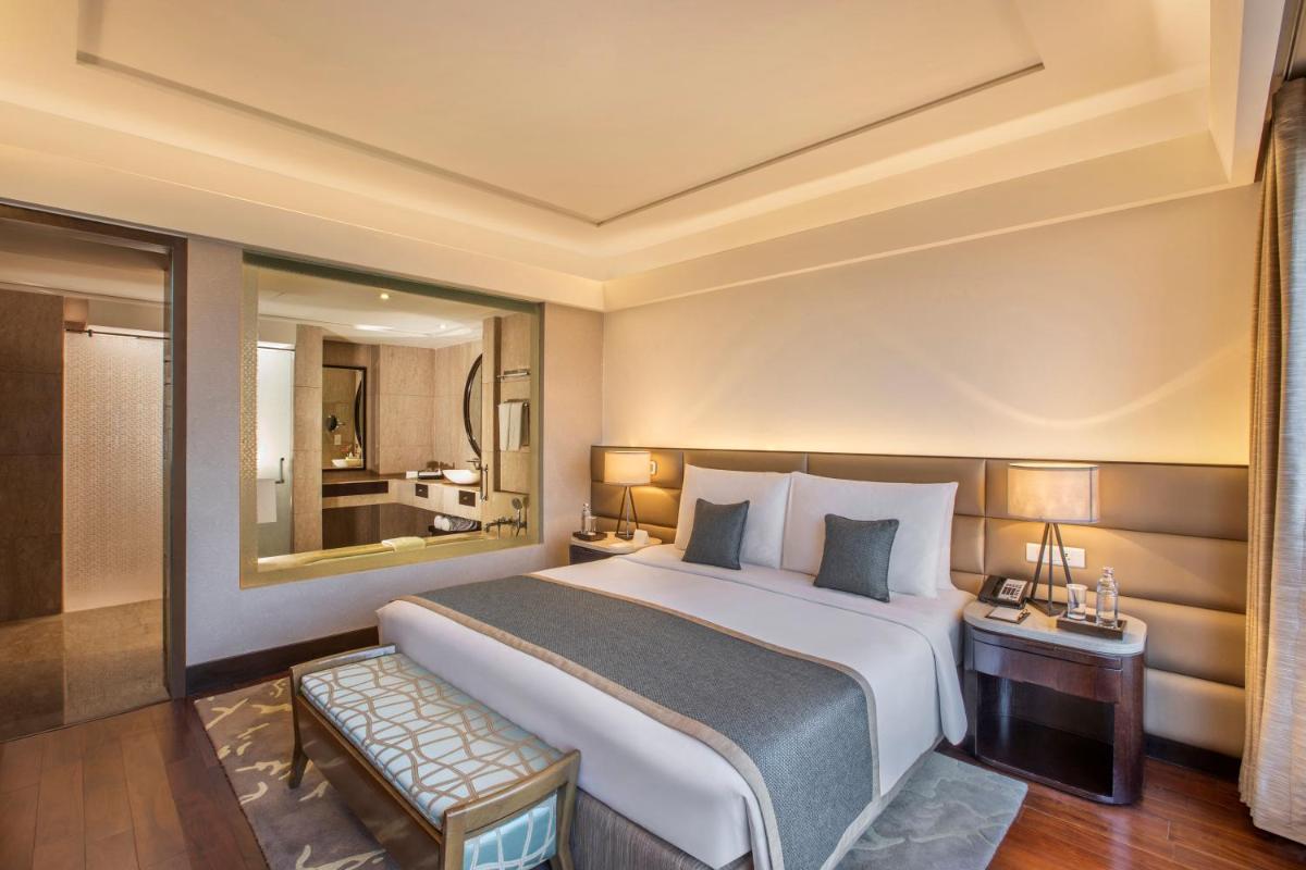 a bedroom with a large bed and a large mirror at The Leela Ambience Convention Hotel Delhi in New Delhi