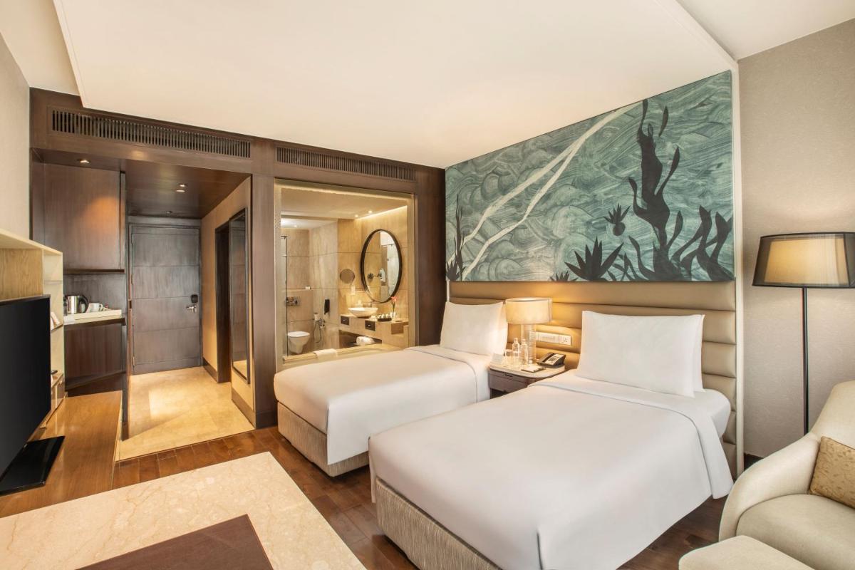 a hotel room with two beds and a couch at The Leela Ambience Convention Hotel Delhi in New Delhi