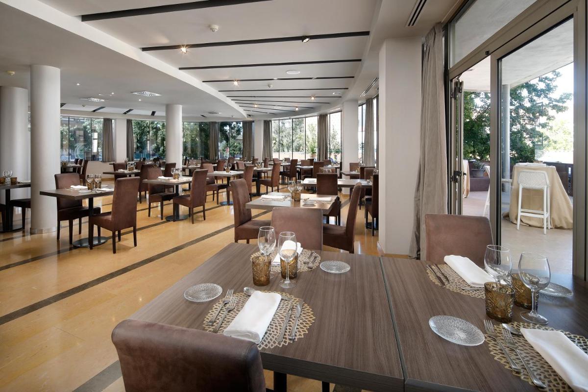 Un restaurante con mesas y sillas de madera y grandes ventanales. en Hotel MasMonzon, en Monzón