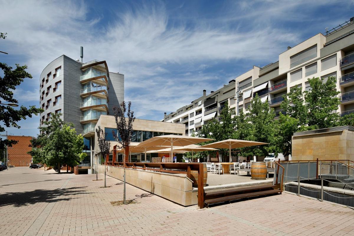un patio con mesas y sombrillas frente a los edificios en Hotel MasMonzon, en Monzón