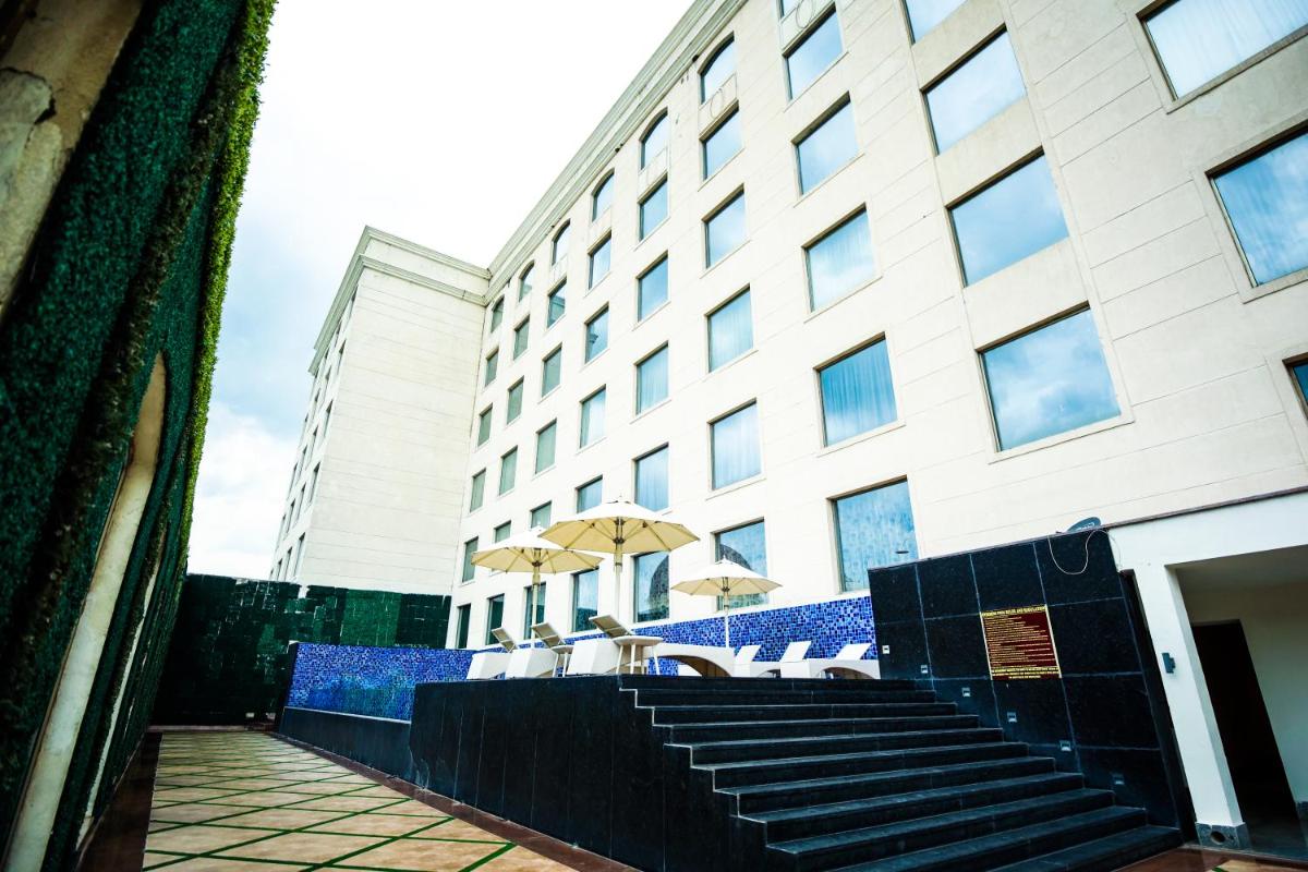 a building with tables and umbrellas in front of it at Ramada Plaza by Wyndham Lucknow in Lucknow