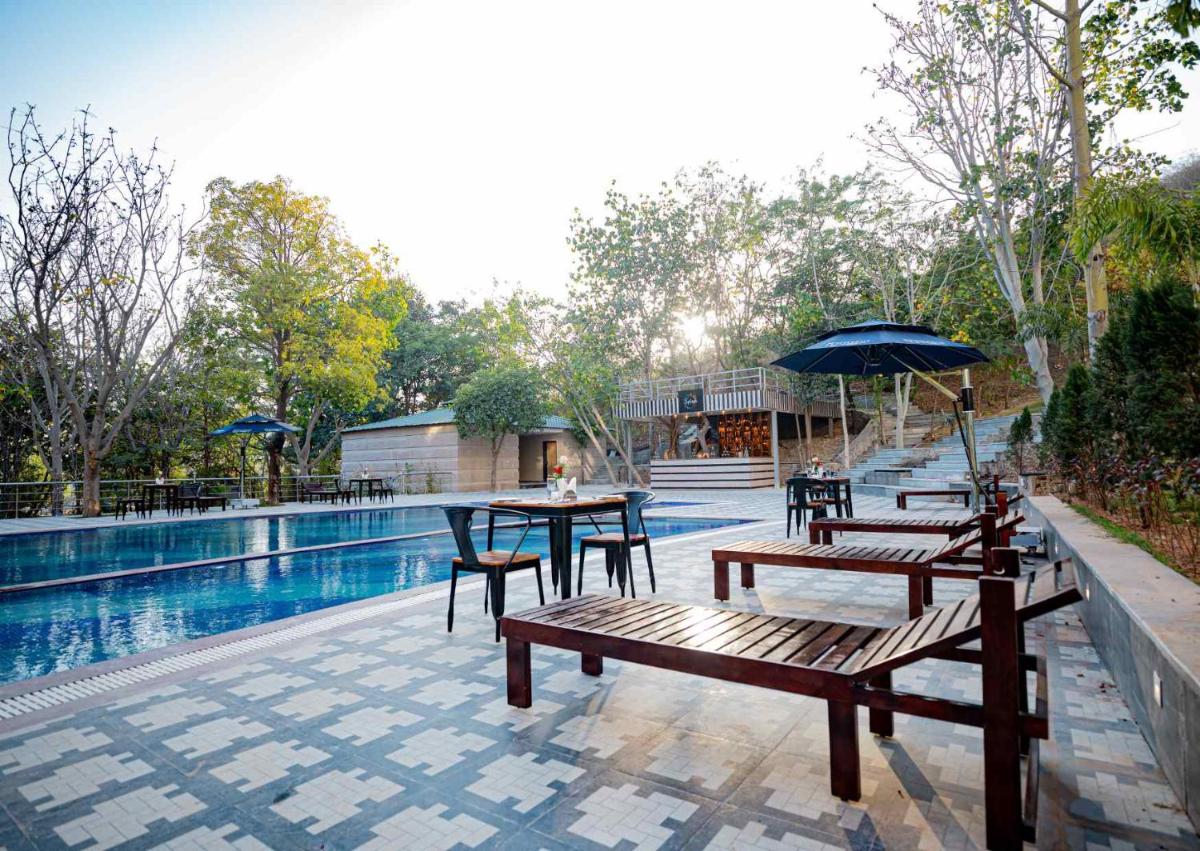 a patio with tables and benches next to a pool at Essentia Luxury Resort & Spa Udaipur in Udaipur