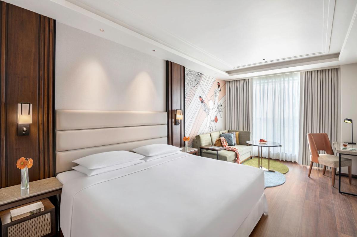 a bedroom with a large white bed and a living room at Hyatt Centric Rajpur Road Dehradun in Dehradun