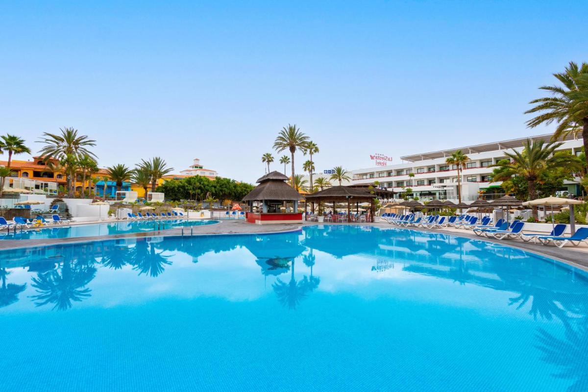 Una gran piscina con sillas y un hotel. en Alexandre La Siesta, en Playa de las Américas
