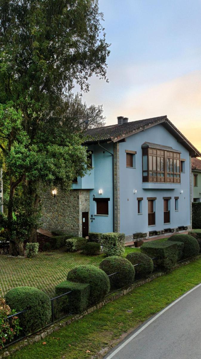 una casa blanca con un árbol y arbustos en LA CASONA Encanto Rural - ApartaHotel SPA Llanes, en Llanes