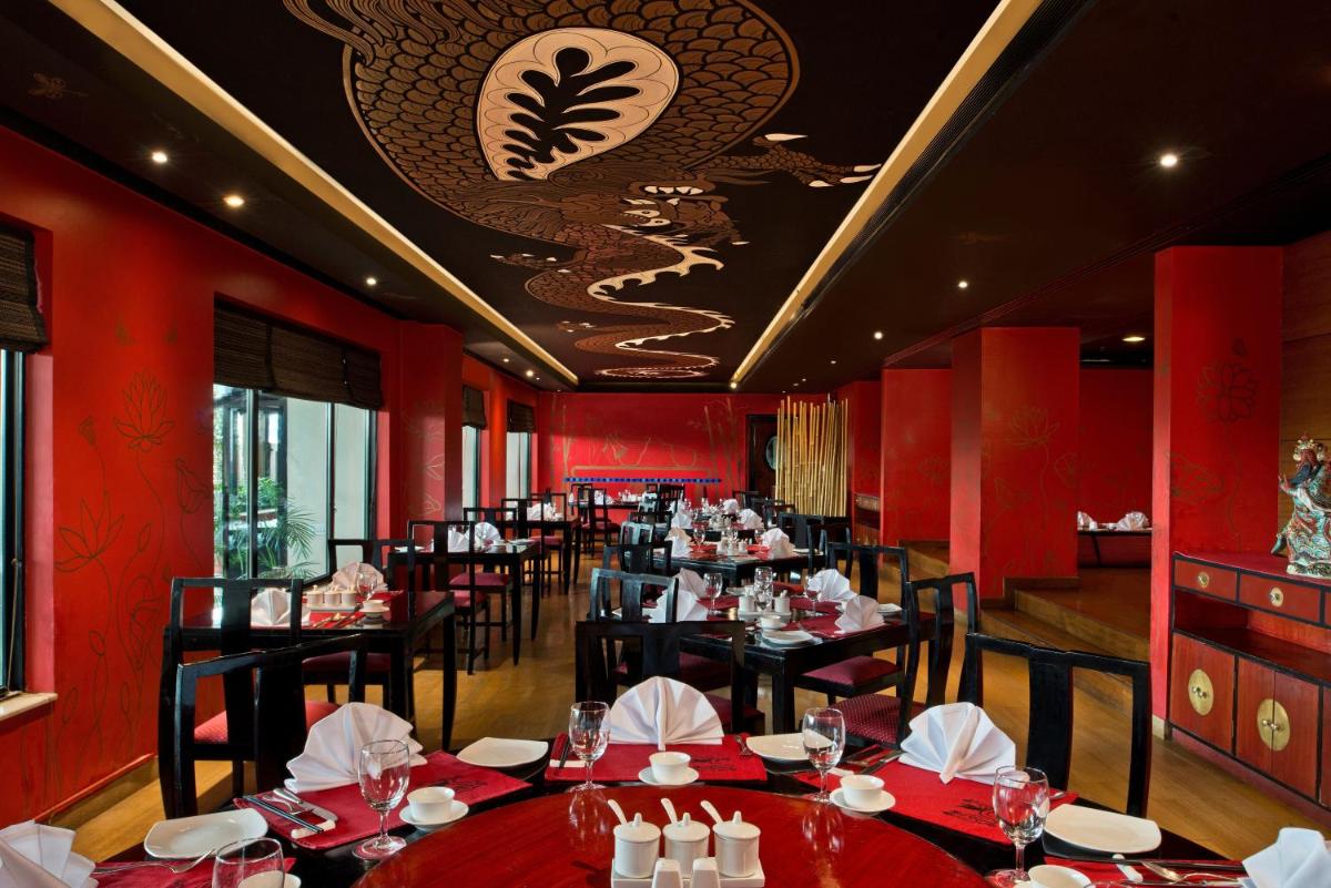a restaurant with red walls and black tables and chairs at Radisson Jaipur City Center in Jaipur