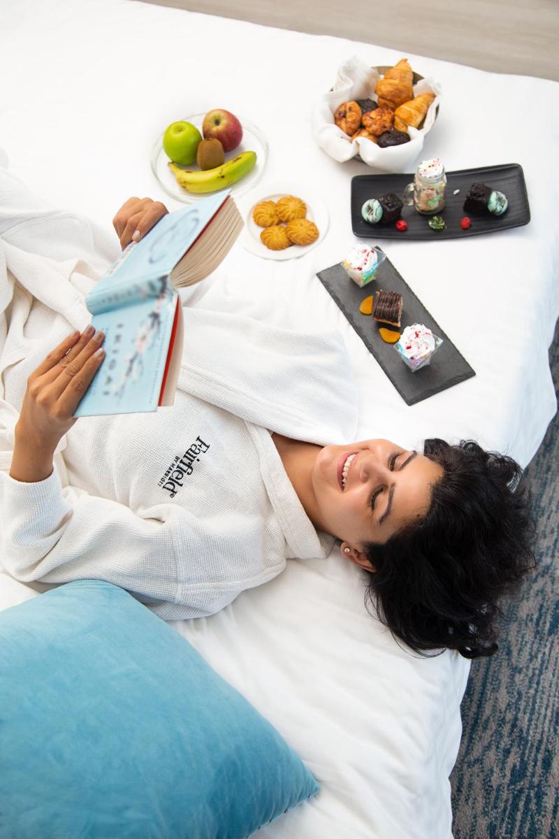 a woman laying on a bed with a plate of food at Fairfield by Marriott Dehradun in Dehradun