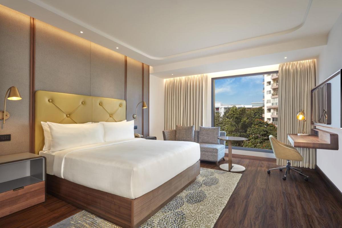a hotel room with a bed and a desk and a window at Doubletree By Hilton Bengaluru Whitefield in Bengaluru