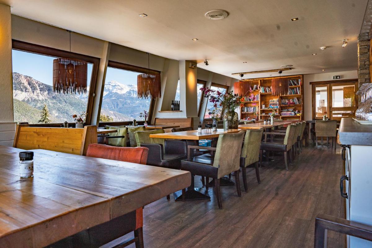 un restaurant avec des tables et des chaises, les montagnes en arrière-plan dans l'établissement Hôtel Restaurant Saint Roch, à Puy-Saint-Vincent