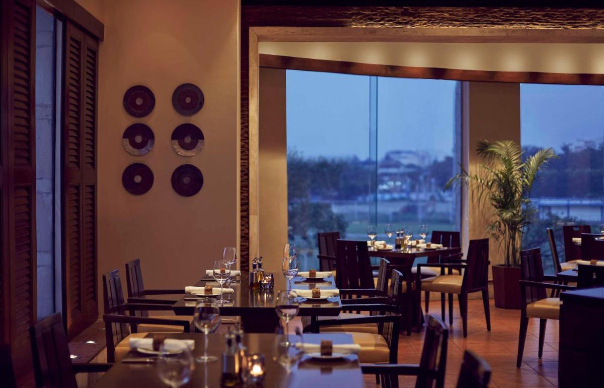 a restaurant with tables and chairs and a large window at Hyatt Regency Kolkata in Kolkata a restaurant with tables and chairs and a large window at Hyatt Regency Kolkata in Kolkata