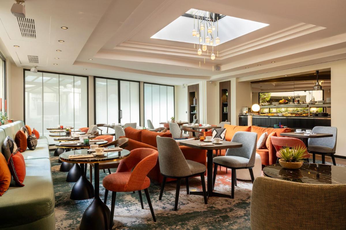 un restaurant avec des chaises orange, des tables et des fenêtres dans l'établissement Hôtel Etoile Maillot, à Paris
