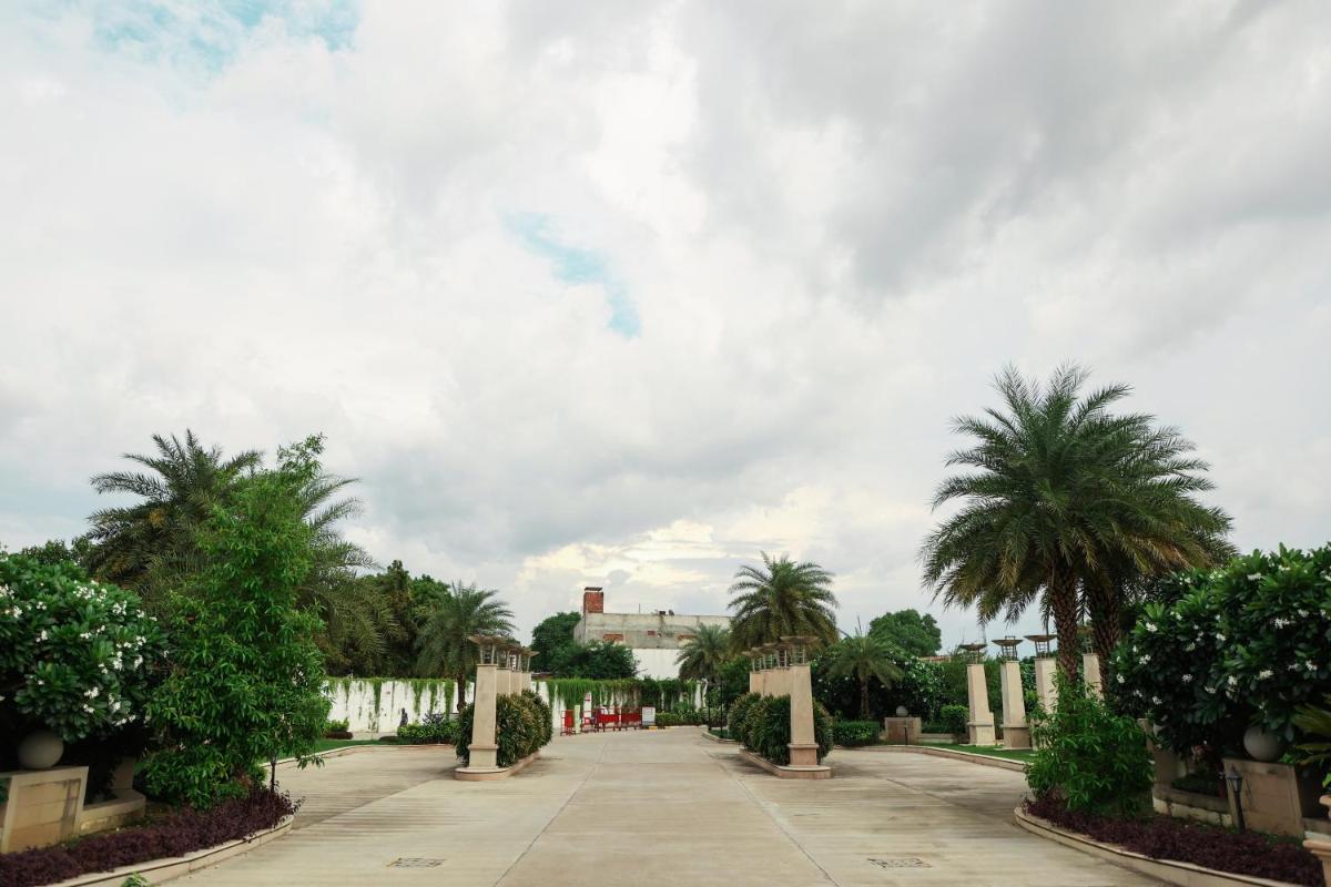 a walkway with palm trees and a cloudy sky at Ramada by Wyndham Lucknow Hotel and Convention Center in Lucknow