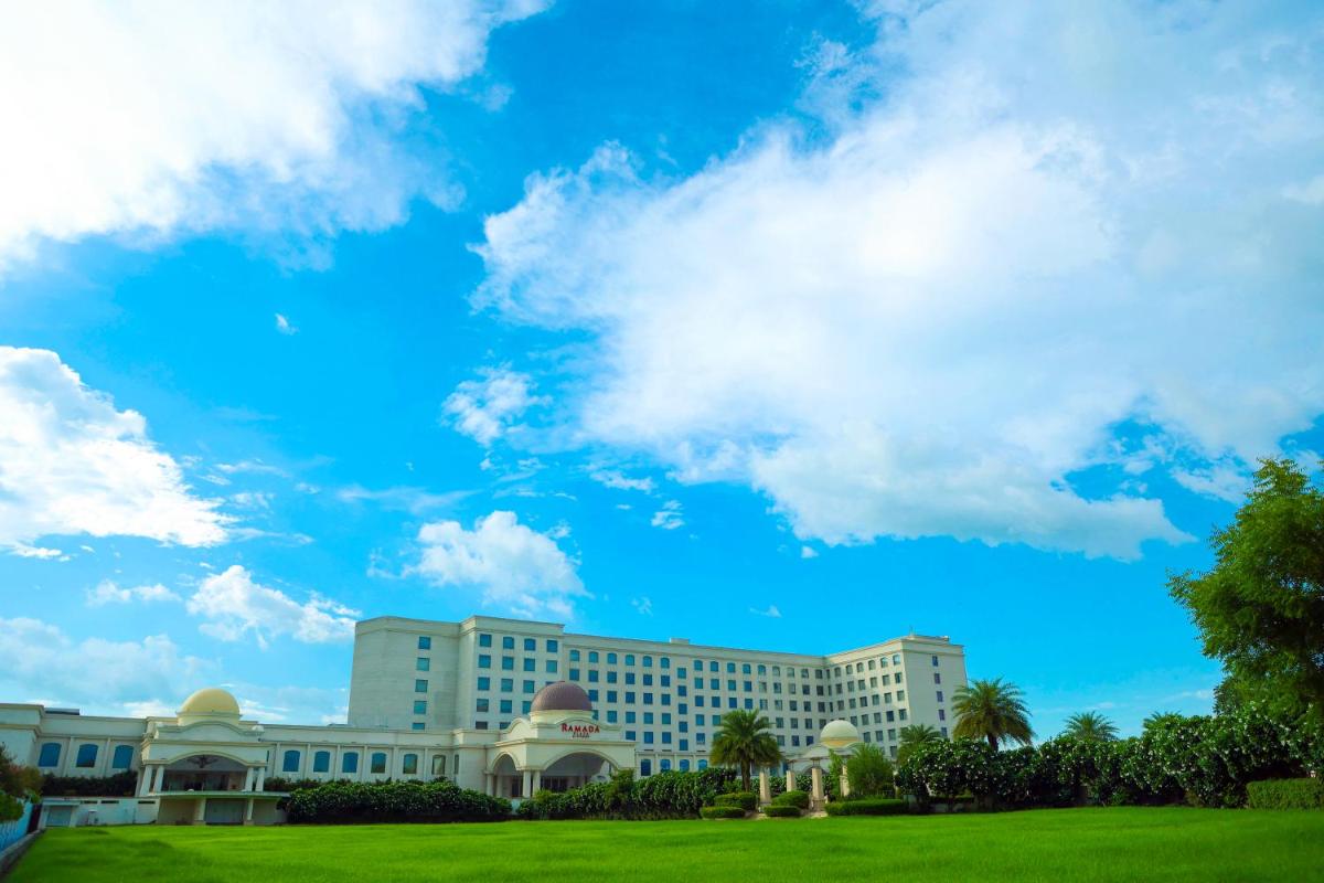 a large white building with a blue sky and clouds at Ramada by Wyndham Lucknow Hotel and Convention Center in Lucknow