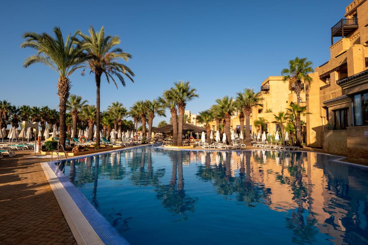 Una gran piscina con palmeras y edificios. en Vila Gale Isla Canela, en Isla Canela