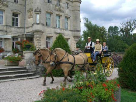deux personnes voyageant en calèche devant un bâtiment dans l'établissement Château des Monthairons Hôtel Restaurant GastroMaison Spa privatif, à Les Monthairons
