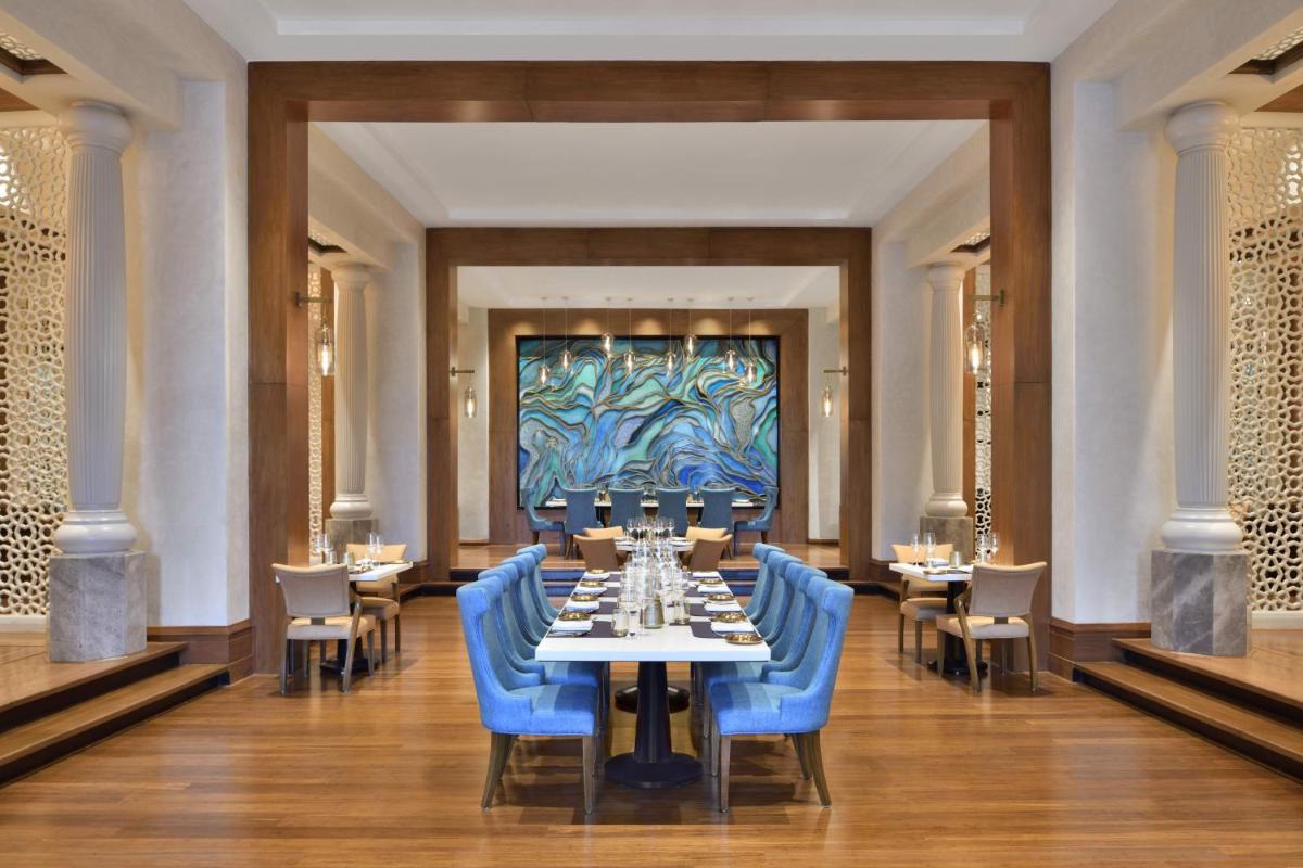 a dining room with tables and blue chairs and a painting at The Westin Mumbai Powai Lake in Mumbai