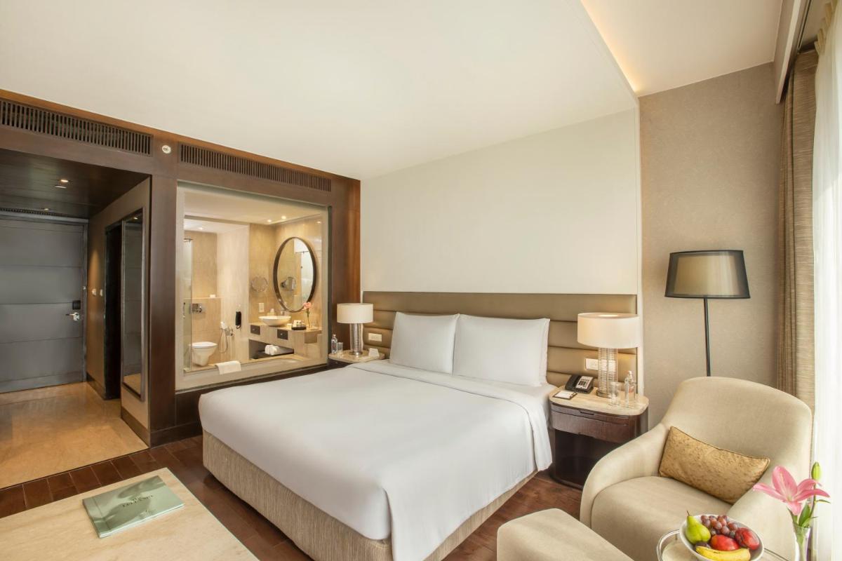 a bedroom with a large white bed and a chair at The Leela Ambience Convention Hotel Delhi in New Delhi