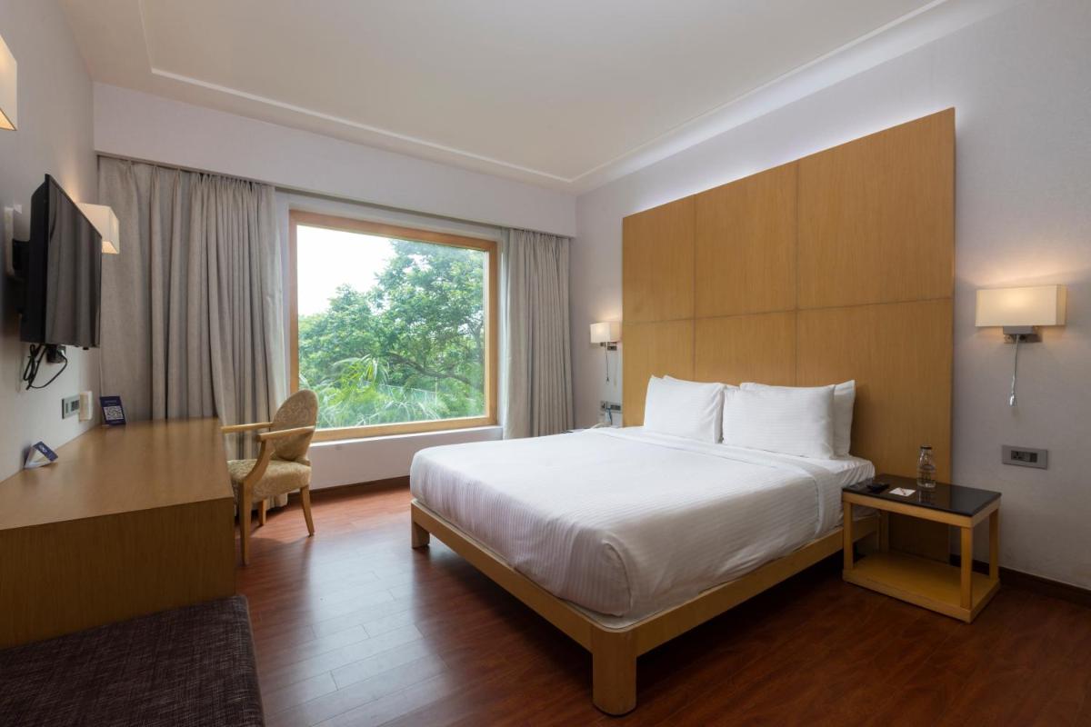 a hotel room with a bed and a desk and a window at Novotel Hyderabad Airport in Hyderabad