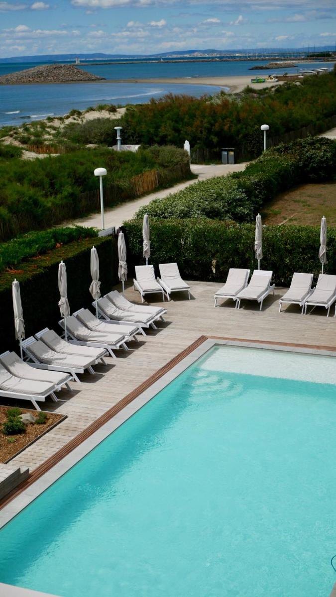 une piscine avec des chaises longues et un tas de visières dans l'établissement Hôtel La Plage 5 étoiles La Grande Motte, à La Grande Motte