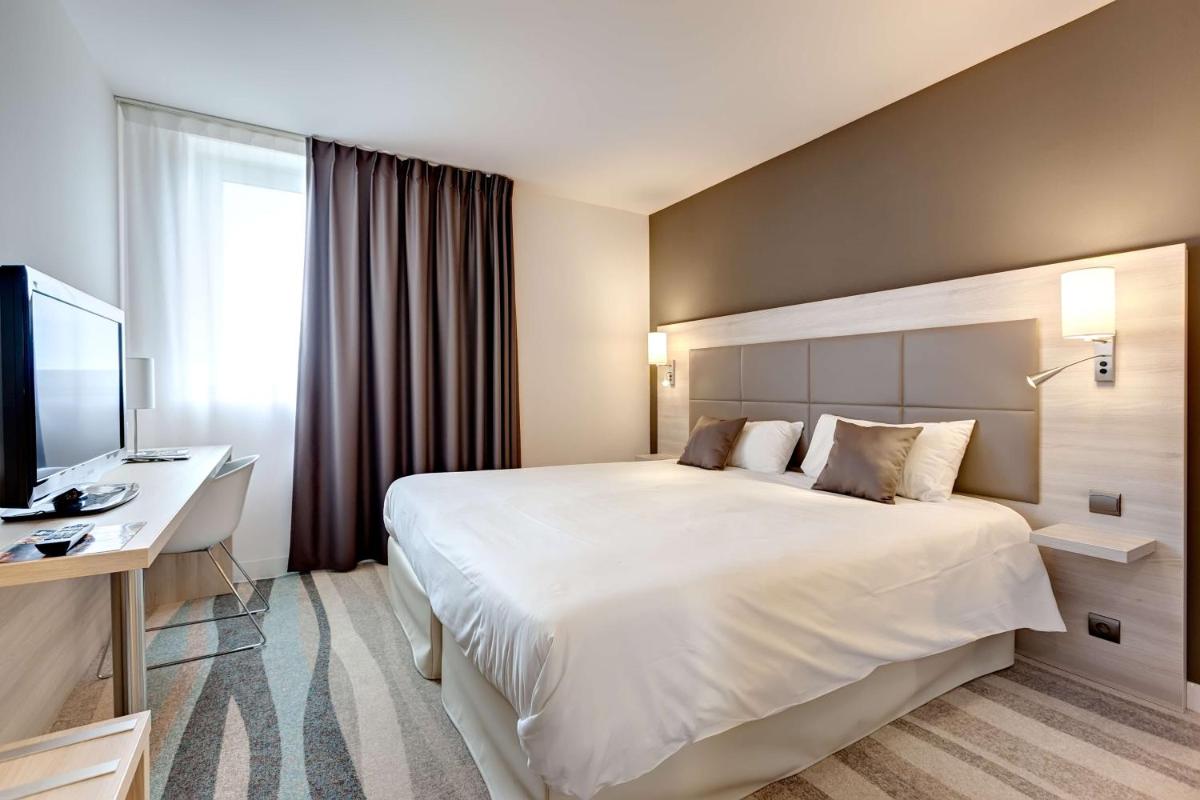 une chambre d'hôtel avec un grand lit blanc et un bureau dans l'établissement Brit Hotel Vendée Mer, à La Mothe-Achard