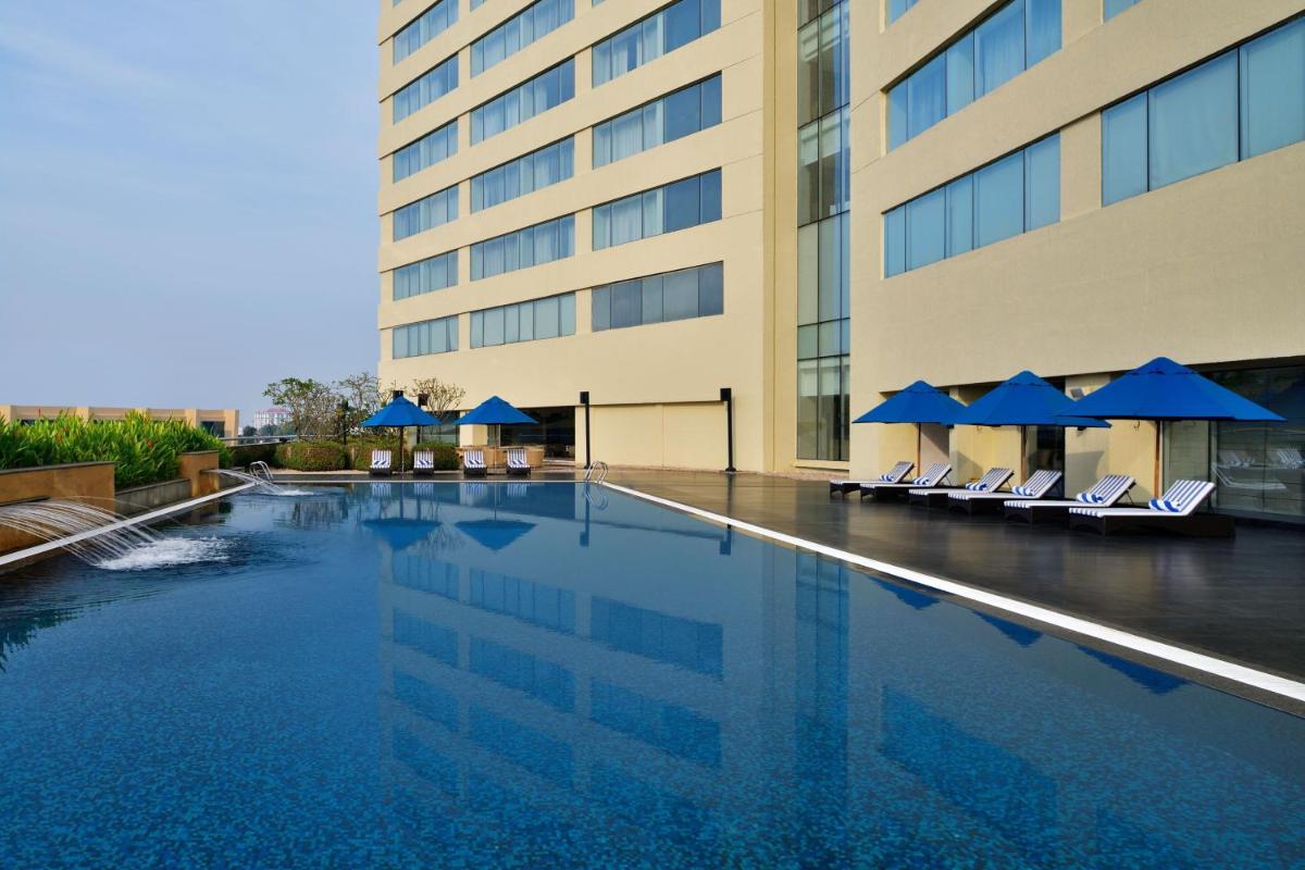 a swimming pool in front of a building with chairs and umbrellas at Kochi Marriott Hotel in Cochin
