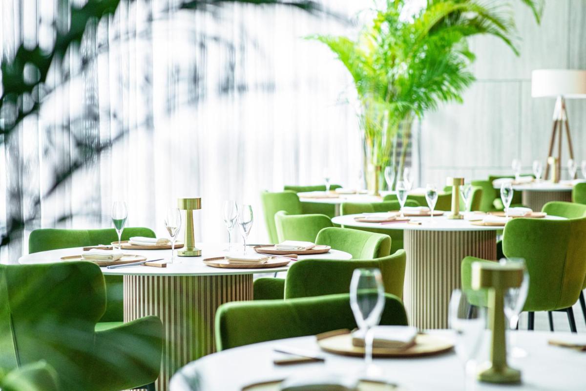 a restaurant with white tables and green chairs at Capri by Fraser China Square, Singapore in Singapore