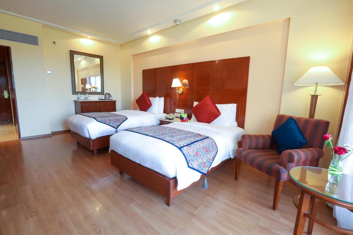 a hotel room with two beds and a chair at The Lalit Mumbai in Mumbai