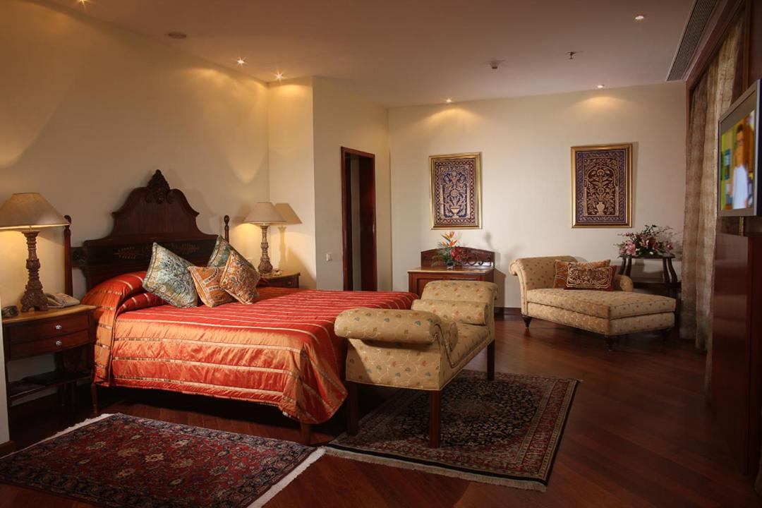 a bedroom with a bed and a chair and a couch at The Lalit Mumbai in Mumbai