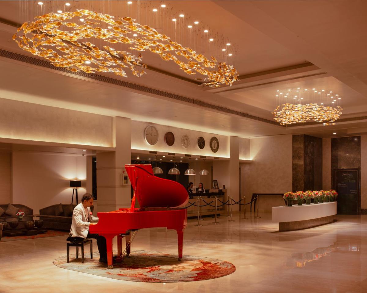 a man sitting in a chair next to a red piano at Radisson Blu Bengaluru Outer Ring Road in Bengaluru