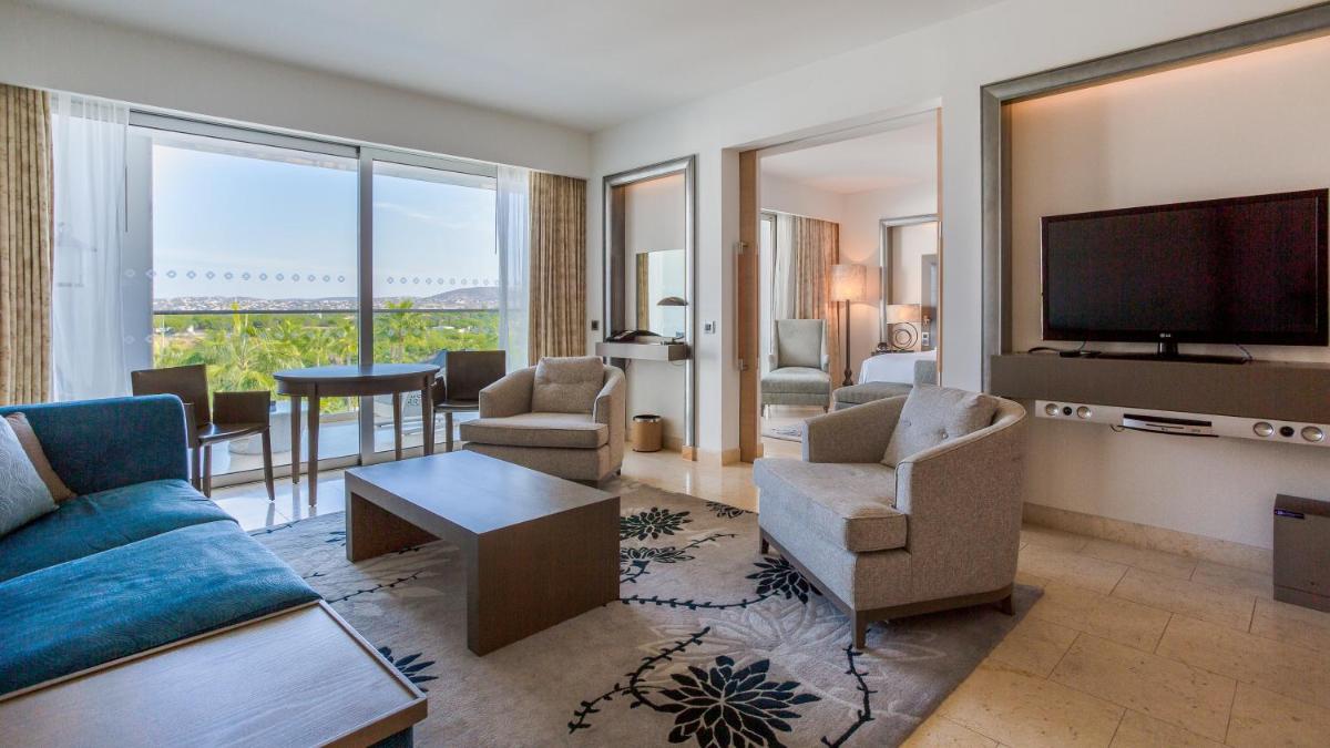 uma sala de estar com um sofá, cadeiras e uma televisão em Conrad Algarve na Quinta do Lago
