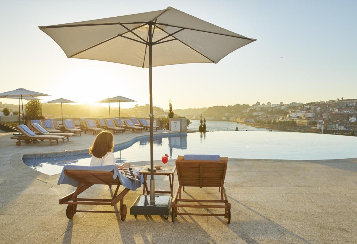 uma mulher sentada em cadeiras debaixo de um guarda-sol ao lado de uma piscina em The Yeatman em Vila Nova de Gaia