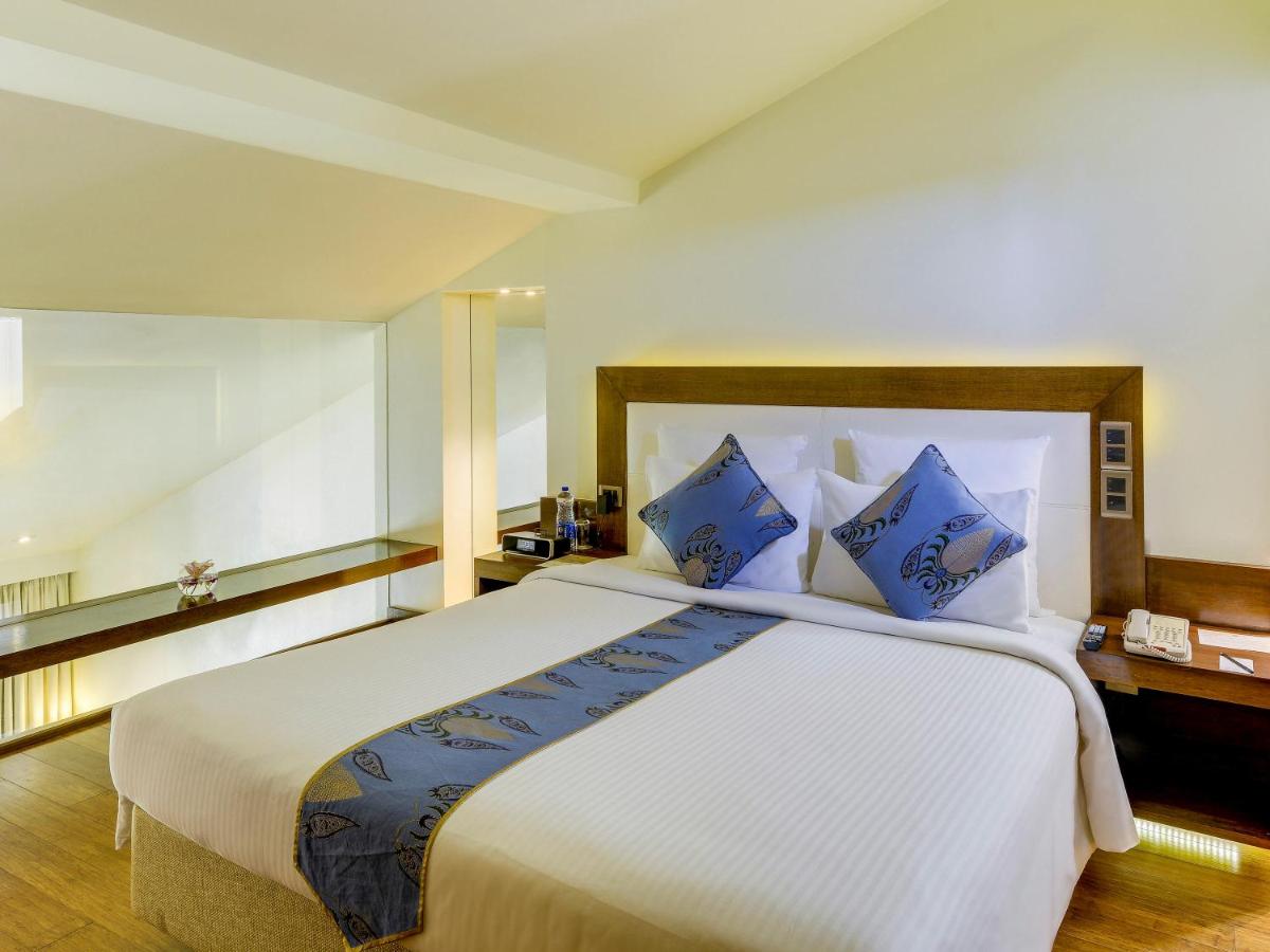a bedroom with a large white bed with blue pillows at Novotel Goa Candolim in Candolim a bedroom with a large white bed with blue pillows at Novotel Goa Candolim in Candolim