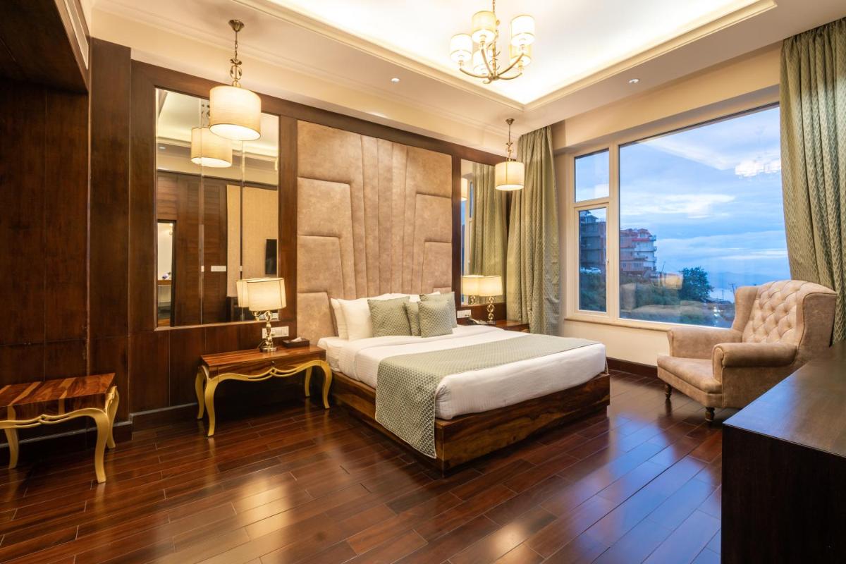 a bedroom with a bed and a chair and a window at The Orchid Shimla in Shimla