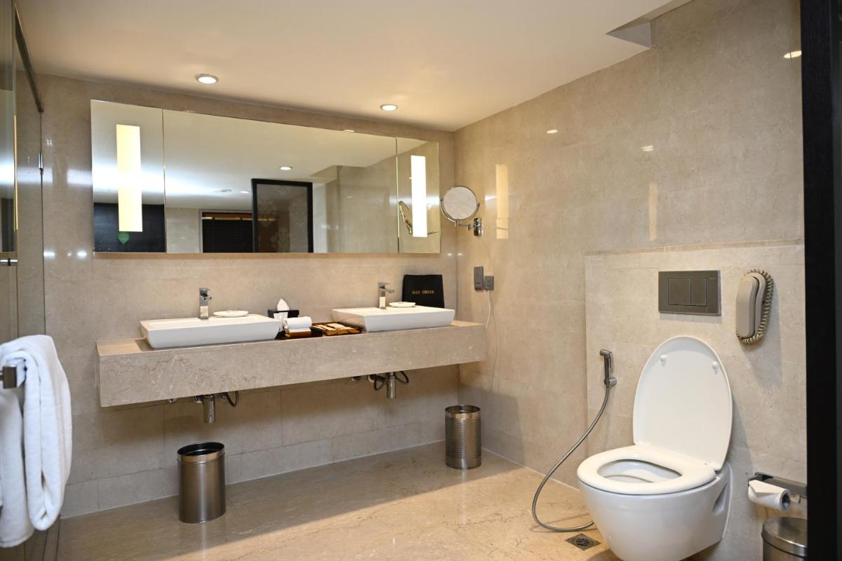 a bathroom with two sinks and a toilet and a mirror at The LaLiT New Delhi in New Delhi