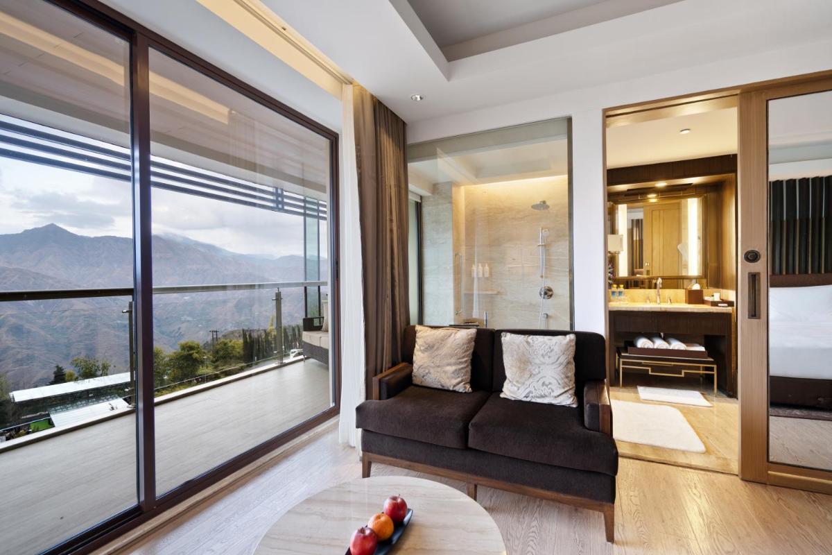 a living room with a couch and a large window at JW Marriott Mussoorie Walnut Grove Resort & Spa in Mussoorie