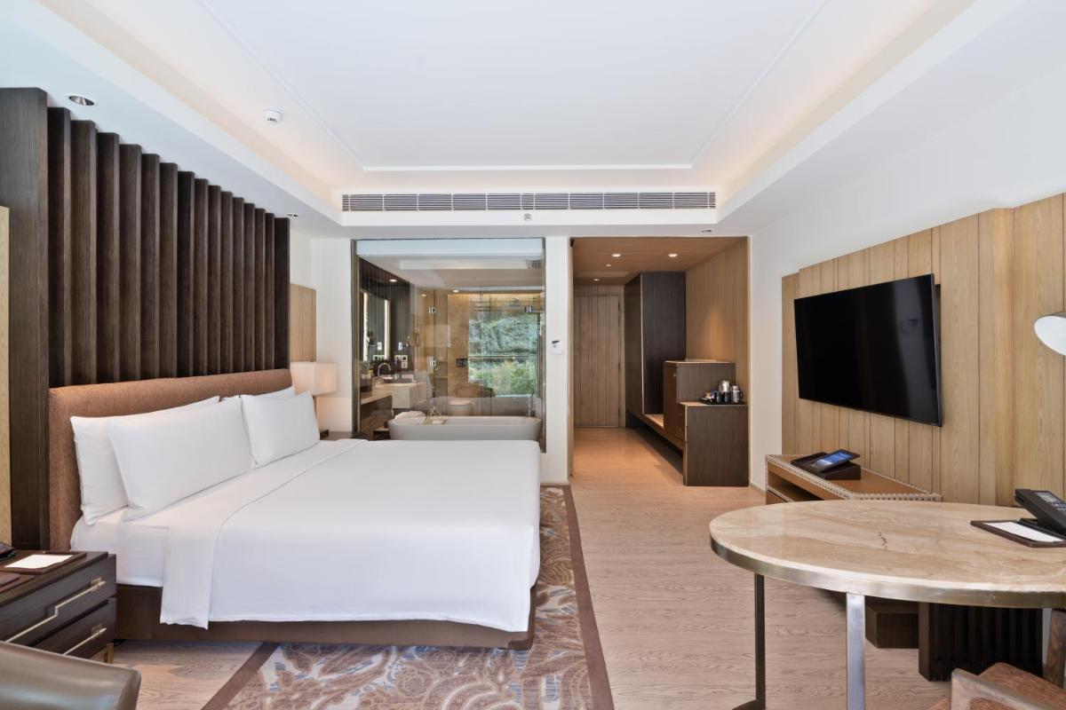 a bedroom with a white bed and a living room at JW Marriott Mussoorie Walnut Grove Resort & Spa in Mussoorie