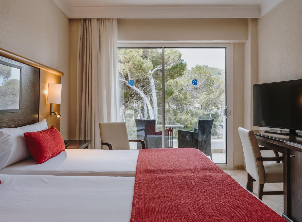 Una habitación de hotel con una cama y una ventana grande. en Grupotel Aguait Resort & Spa - Adults Only, en Cala Ratjada