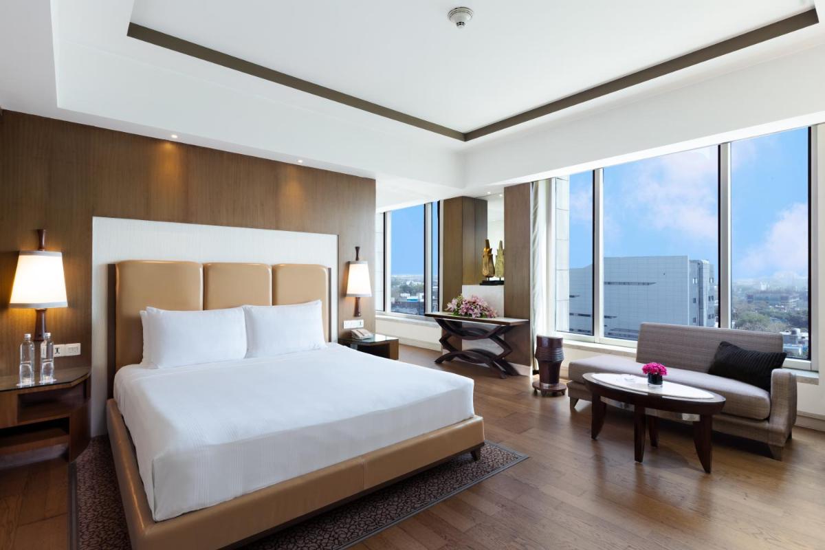 a bedroom with a large white bed and a room with windows at Crowne Plaza New Delhi Okhla by IHG in New Delhi