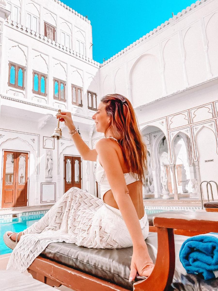 a woman sitting on a bed in front of a pool at The Raj Palace (Small Luxury Hotels of the World) in Jaipur