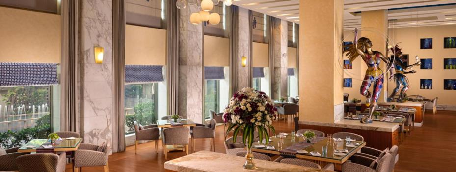 a restaurant with tables and chairs and flowers in a room at Jaypee Vasant Continental in New Delhi
