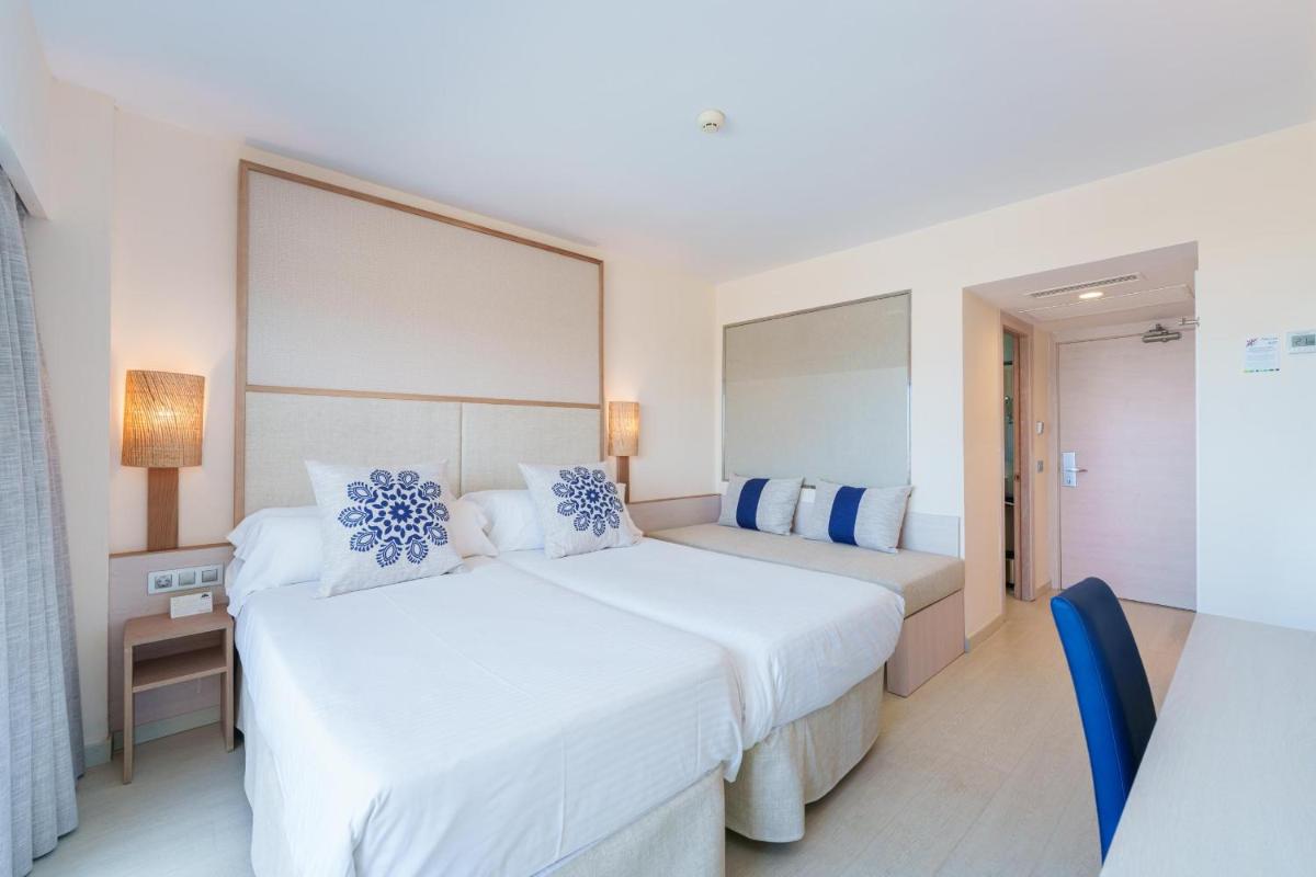 Dos camas en una habitación de hotel con almohadas blancas y azules. en Ferrer Janeiro Hotel & Spa, en Can Picafort