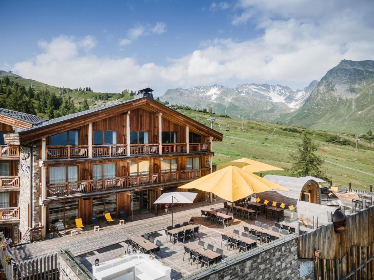 un bâtiment avec des tables et des parasols devant lui dans l'établissement Hôtel Alparena & Spa - 4 étoiles, à La Rosière