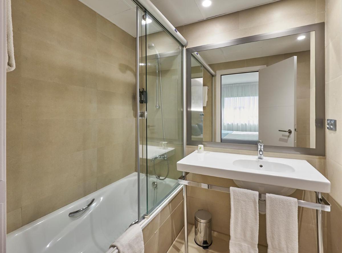 Un baño con lavabo, bañera y espejo. en URH Excelsior, en Lloret de Mar