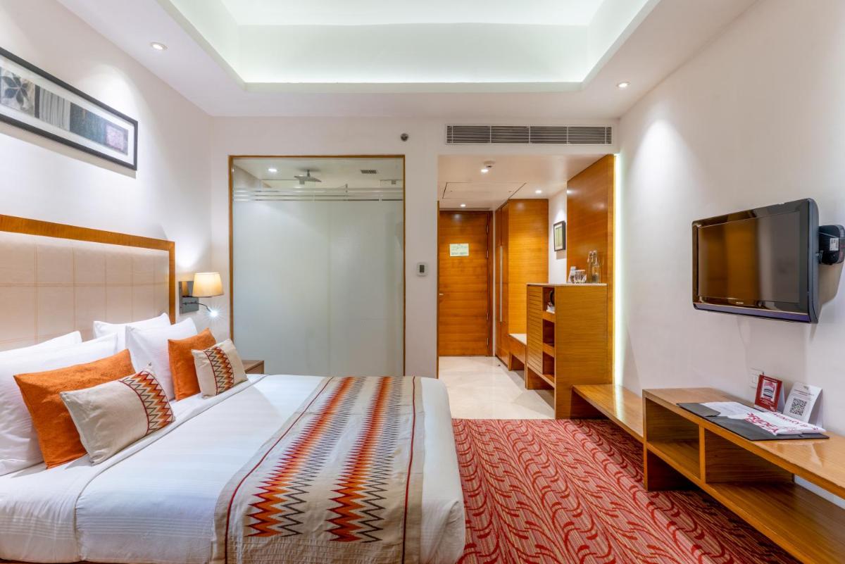 a bedroom with a large bed and a flat screen tv at Pride Plaza Hotel, Kolkata in Kolkata