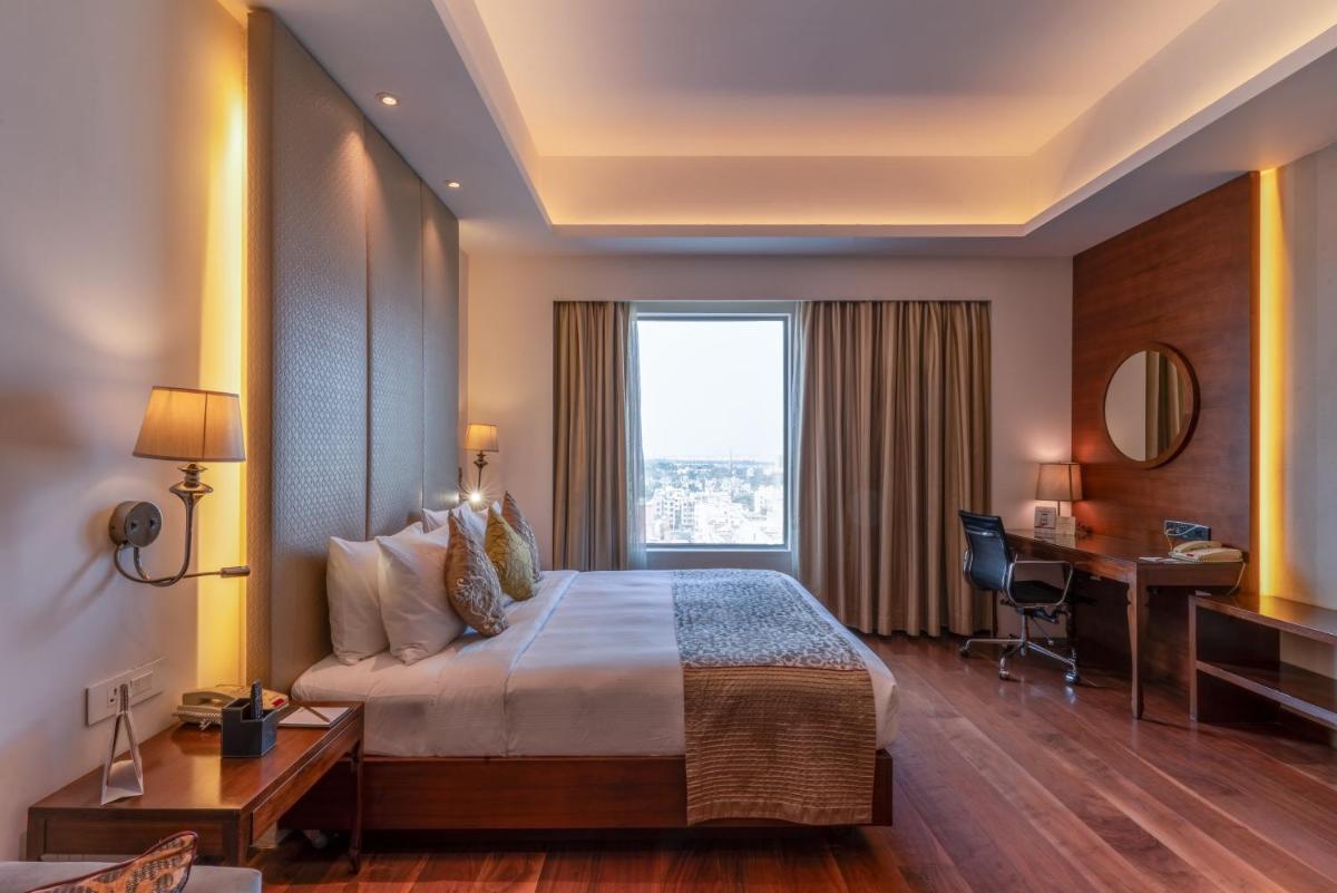 a hotel room with a bed and a desk and a window at Pride Plaza Hotel, Kolkata in Kolkata